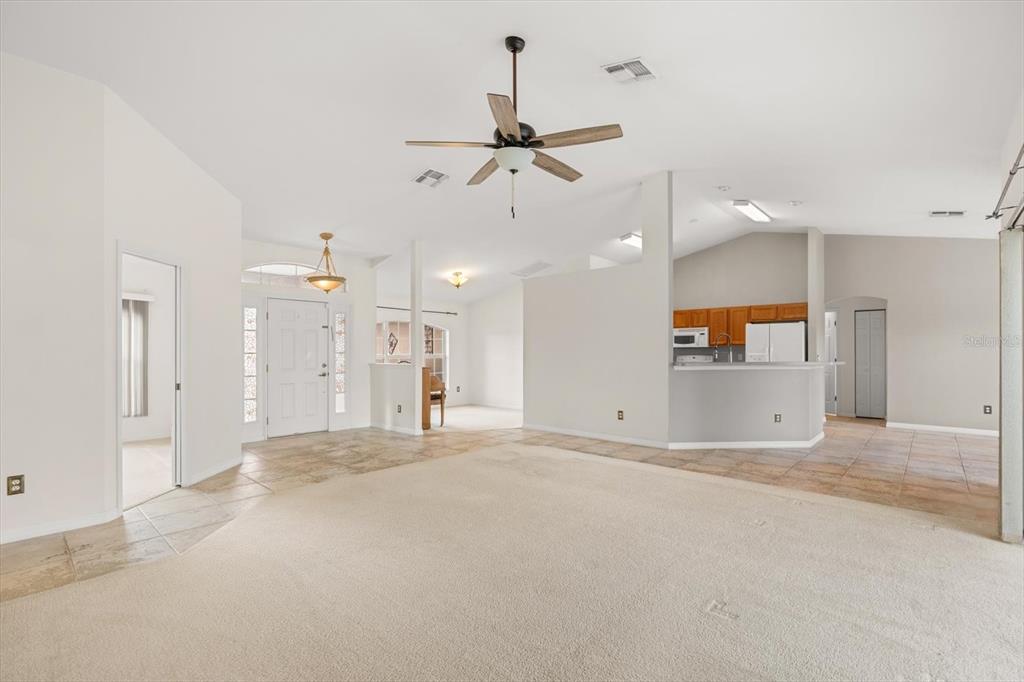 A spacious living room with beige carpet, tile flooring, and an open kitchen in the background — 4910 SW 109TH LOOP, OCALA, FL