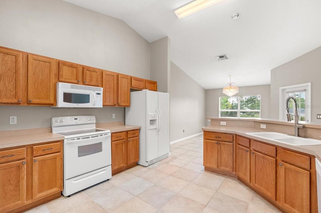 A kitchen features oak cabinets, white appliances, beige countertops, and tile flooring — 4910 SW 109TH LOOP, OCALA, FL