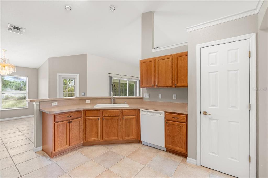 A kitchen features oak cabinets, a white dishwasher, a sink, and beige tile flooring — 4910 SW 109TH LOOP, OCALA, FL