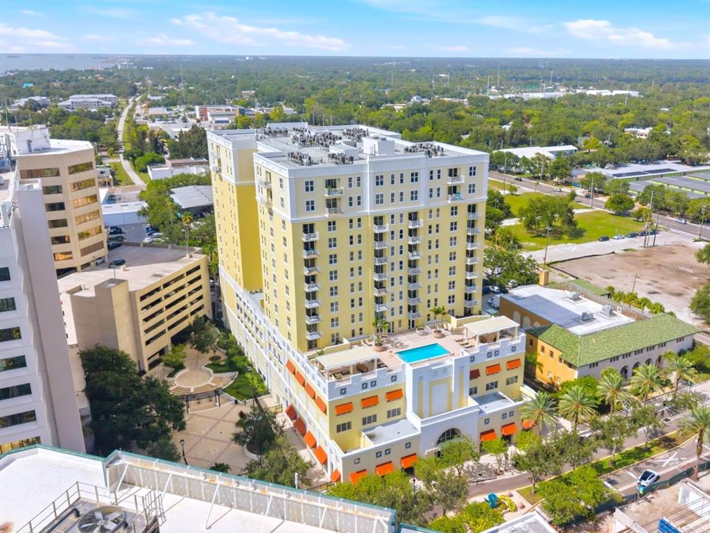 An aerial view shows a multi-story yellow building with a rooftop pool and terrace — 628 CLEVELAND STREET UNIT 1211, CLEARWATER, FL