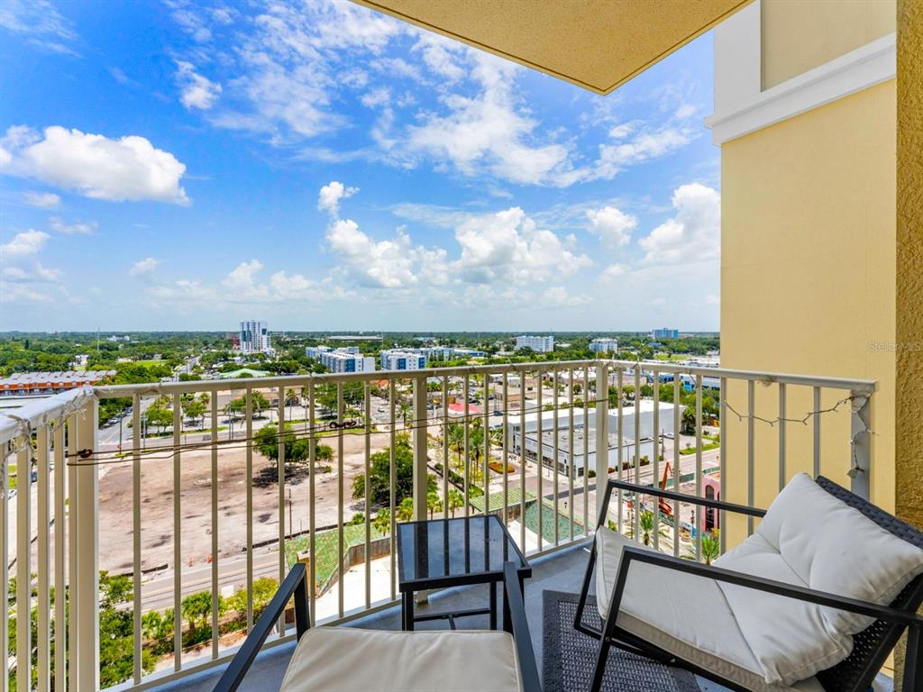 A balcony with two chairs and a small table overlooks a city and landscape view — 628 CLEVELAND STREET UNIT 1211, CLEARWATER, FL