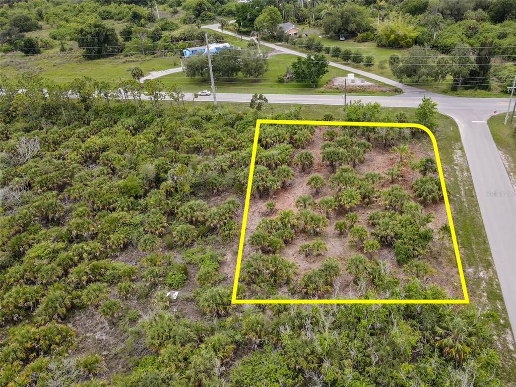 An aerial view shows a vacant, brush-covered lot outlined in yellow next to a road — 25471 TECHNOLOGY BOULEVARD, PUNTA GORDA, FL
