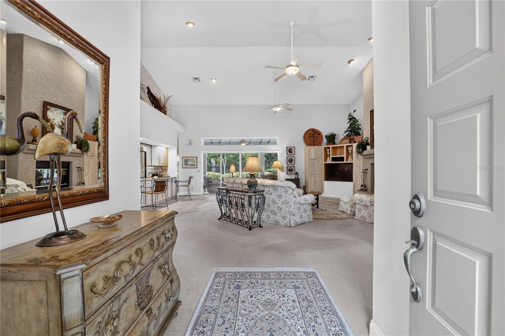 An entryway opens into a spacious living room with vaulted ceilings, carpeted floors, and furniture — 7759 SE 12TH CIRCLE, OCALA, FL