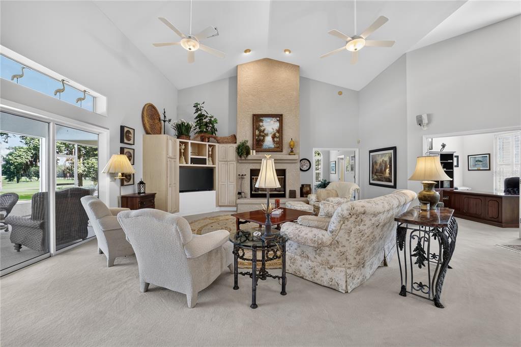 A spacious living room features a vaulted ceiling, a stone fireplace, and large sliding glass doors — 7759 SE 12TH CIRCLE, OCALA, FL