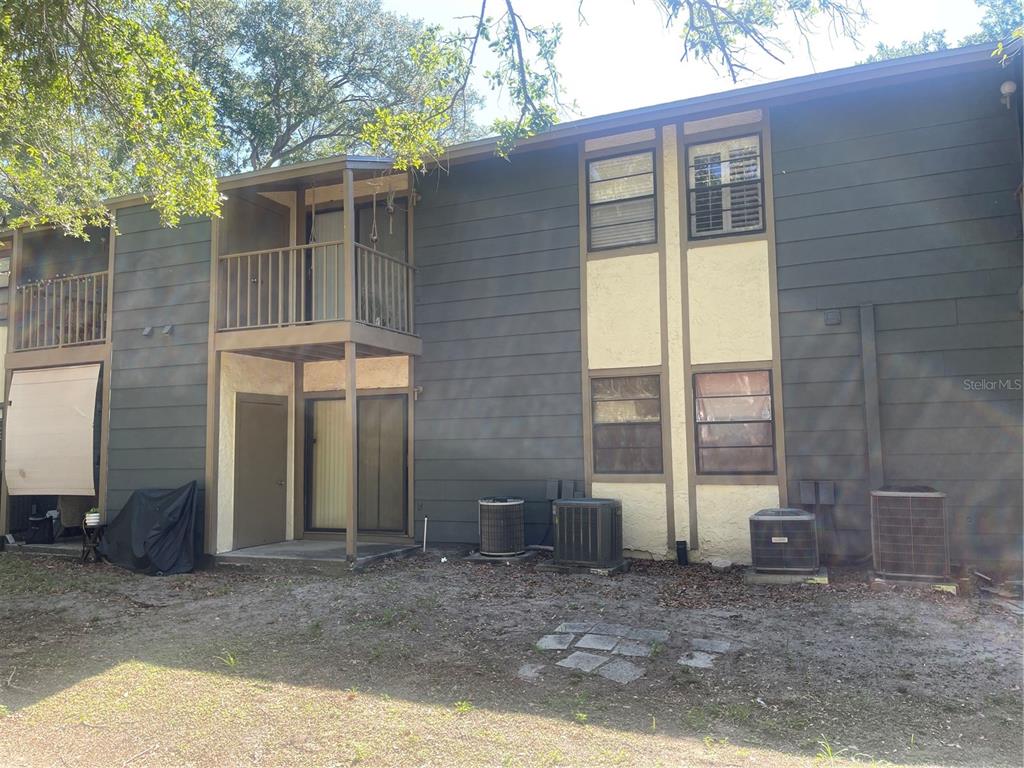 The exterior of a two-story apartment building features dark siding, balconies, and ground-level air conditioning units — 4809 S MOUND AVENUE UNIT 105, TAMPA, FL