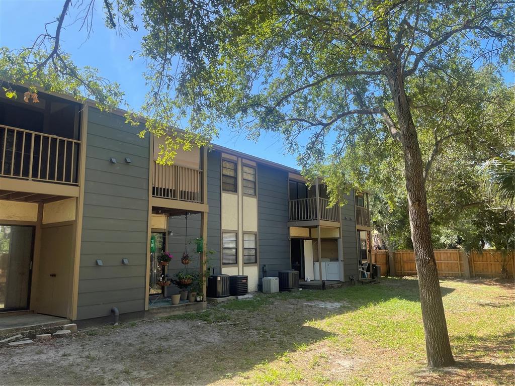 A two-story apartment building with dark siding, balconies, and ground-level patios faces a grassy yard — 4809 S MOUND AVENUE UNIT 105, TAMPA, FL