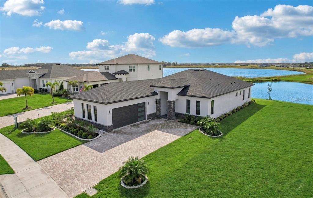 An aerial view of a modern single-story house with a paved driveway and waterfront backyard — 224 VALENCIA RIDGE DRIVE, AUBURNDALE, FL