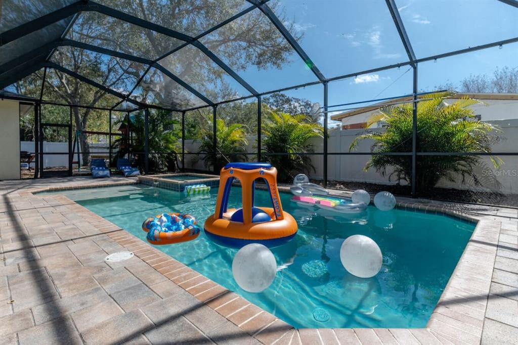 A screened-in swimming pool with a spa and various floating pool toys — 2930 W ROGERS AVENUE, TAMPA, FL