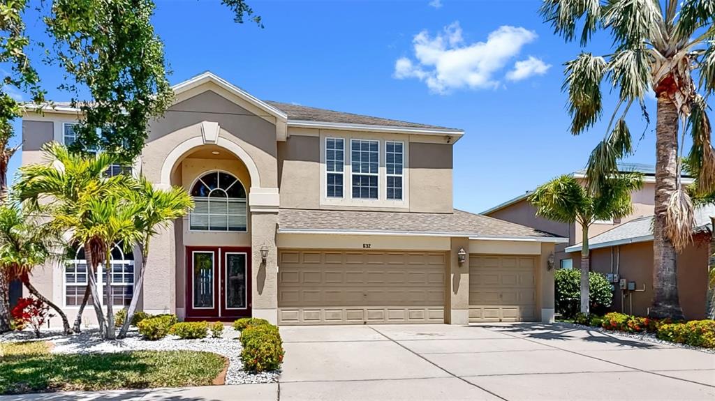 A two-story suburban house with a tan stucco exterior, arched entryway, and three-car garage — 632 TANANA FALL DRIVE, RUSKIN, FL