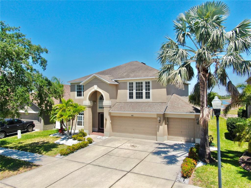 A two-story suburban house with a tan stucco exterior, a three-car garage, and palm trees — 632 TANANA FALL DRIVE, RUSKIN, FL