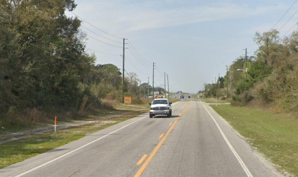 A white pickup truck drives down a two-lane road lined with trees and utility poles — COUNTY LINE ROAD HIGHWAY, HUDSON, FL