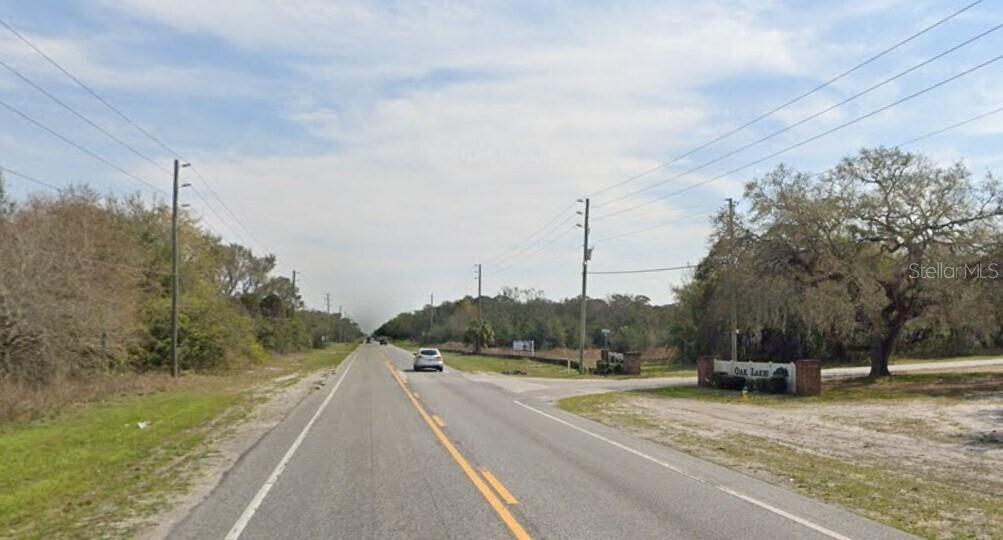 A paved road leads past a sign for Oak Lake with trees on both sides — COUNTY LINE ROAD HIGHWAY, HUDSON, FL