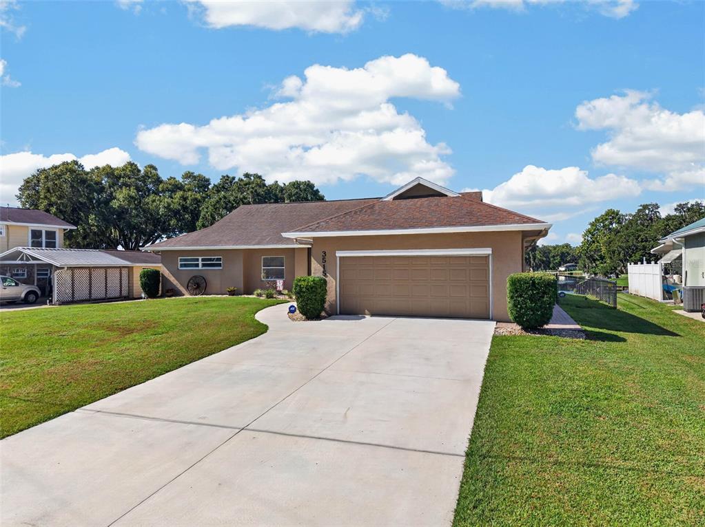 A single-story house with a tan stucco exterior, a two-car garage, and a concrete driveway — 3515 LITTLE LAKE DRIVE, SEBRING, FL