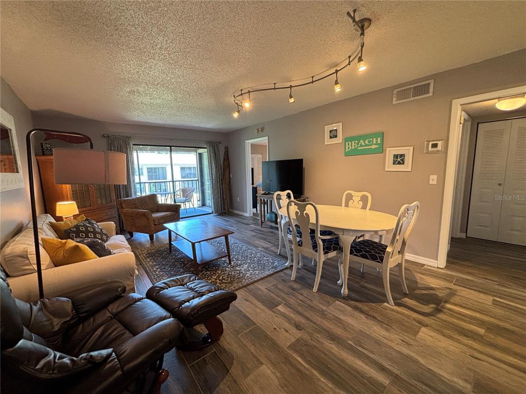 A living and dining area features wood-look tile flooring, track lighting, and a sliding glass door — 204 MEADOW LANE UNIT 204, OLDSMAR, FL