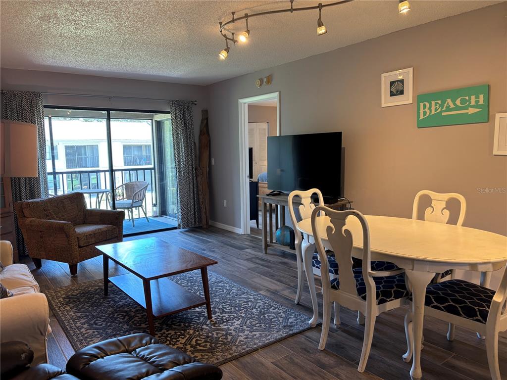 A living and dining area features wood-look flooring, a sliding glass door, and track lighting — 204 MEADOW LANE UNIT 204, OLDSMAR, FL