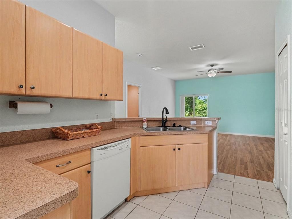 A kitchen with light wood cabinets, laminate countertops, and a dishwasher, opening to a living area — 4288 DUREVE AVENUE, NORTH PORT, FL