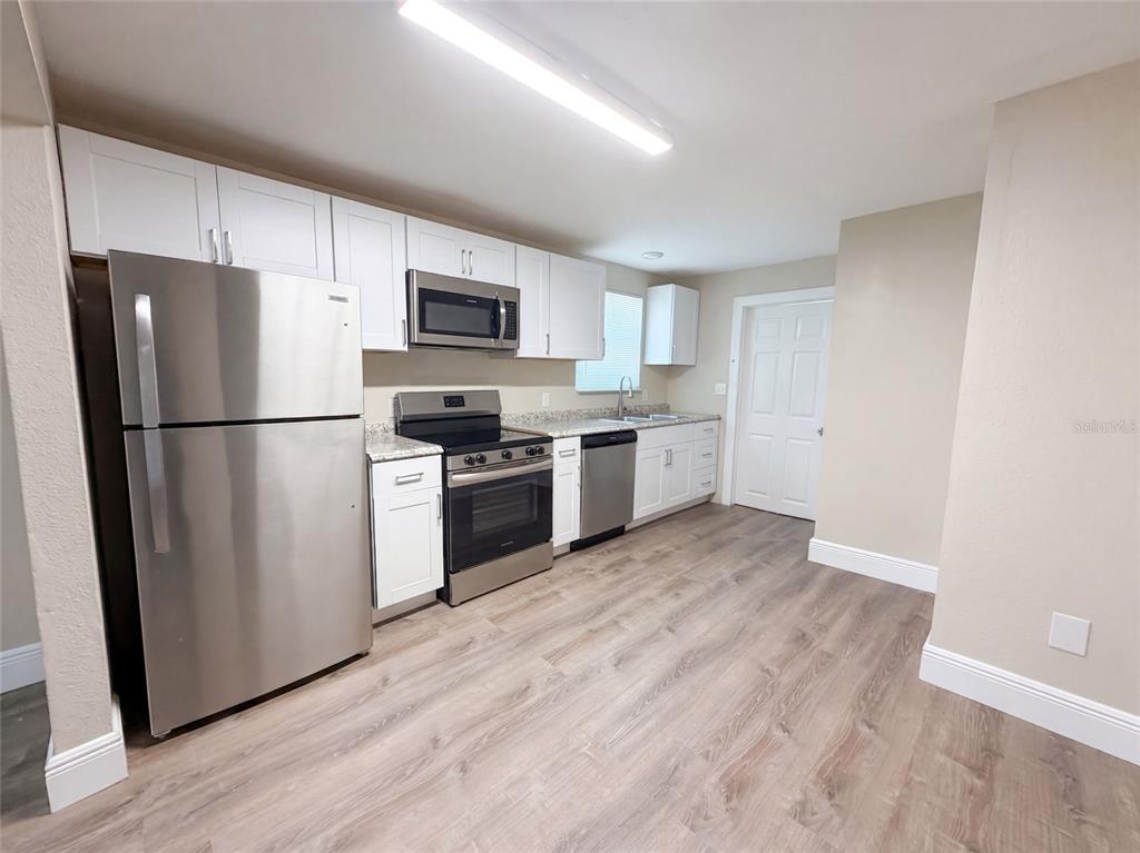 A kitchen features white cabinets, stainless steel appliances, granite countertops, and light wood-look flooring — 8103 N 18TH STREET, TAMPA, FL