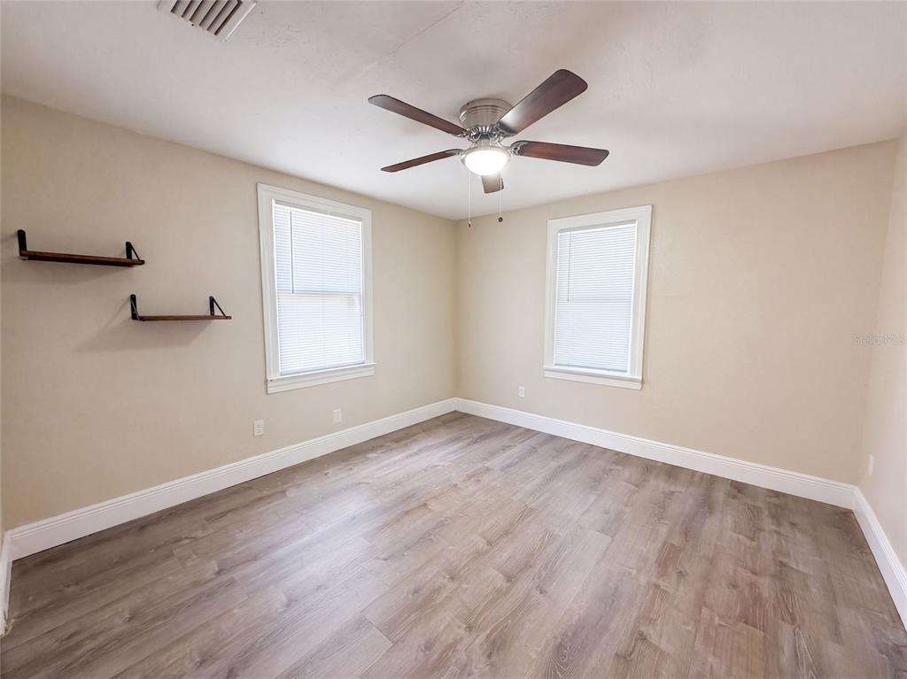 An empty bedroom features light beige walls, wood-look flooring, two windows, and a ceiling fan — 8103 N 18TH STREET, TAMPA, FL