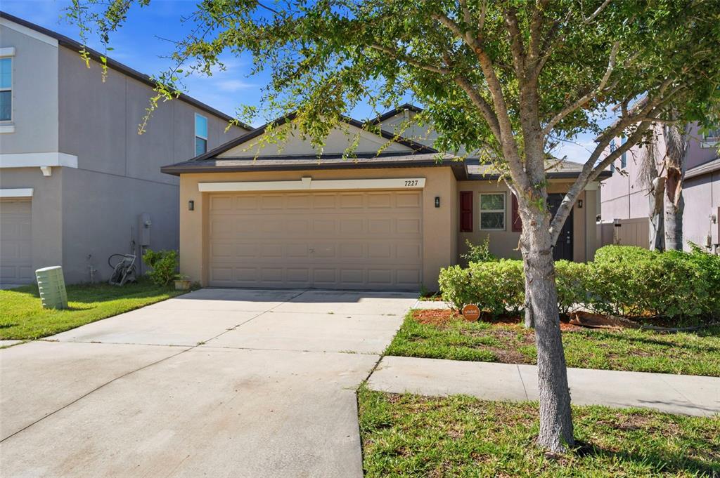A beige single-story house with a two-car garage and a tree in the front yard — 7227 SALT RIVER AVENUE, SUN CITY CENTER, FL