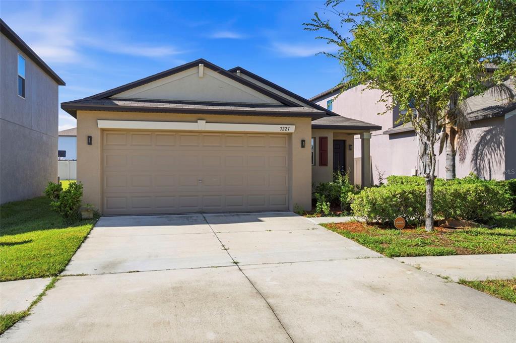 A single-story house with a beige stucco exterior, a two-car garage, and a concrete driveway — 7227 SALT RIVER AVENUE, SUN CITY CENTER, FL