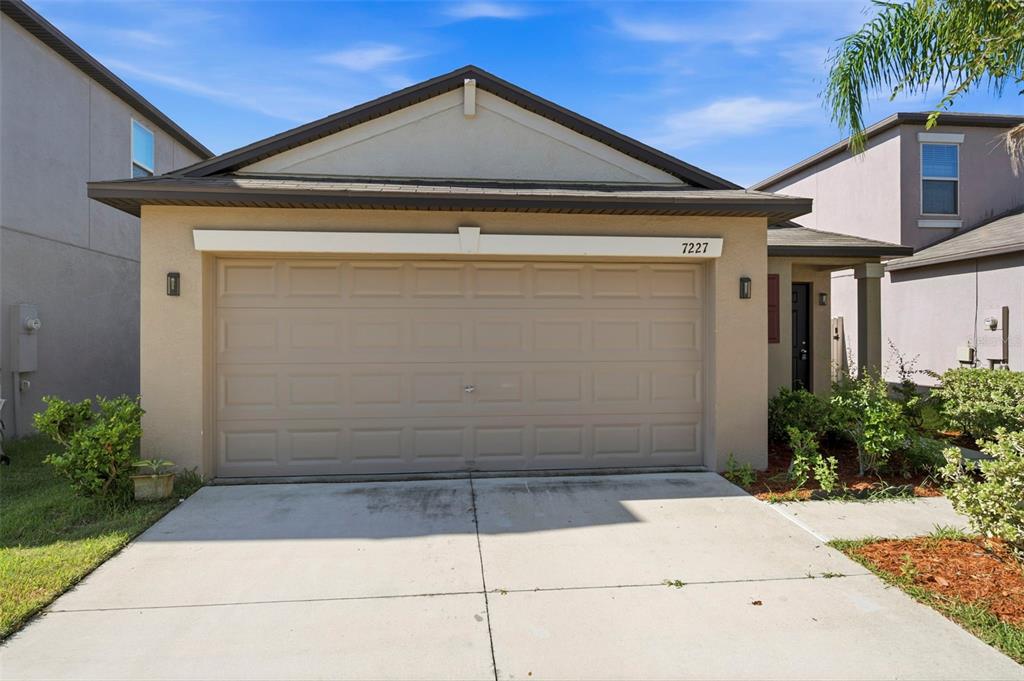 A tan single-story house features a two-car garage and a small front entryway — 7227 SALT RIVER AVENUE, SUN CITY CENTER, FL