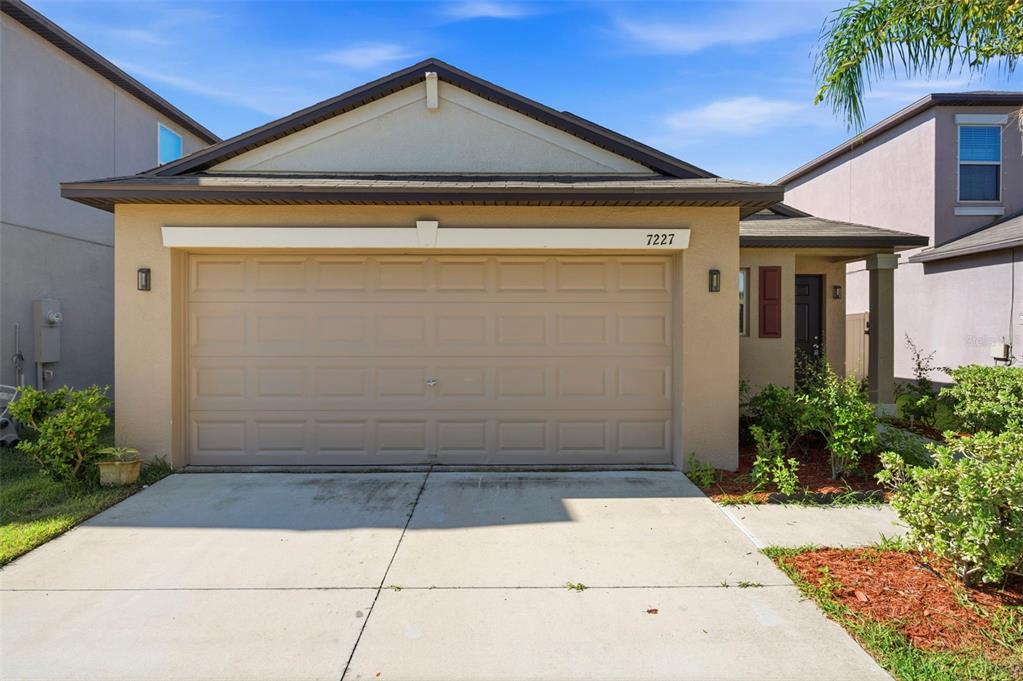 A beige single-story house features a two-car garage and a small front entrance — 7227 SALT RIVER AVENUE, SUN CITY CENTER, FL