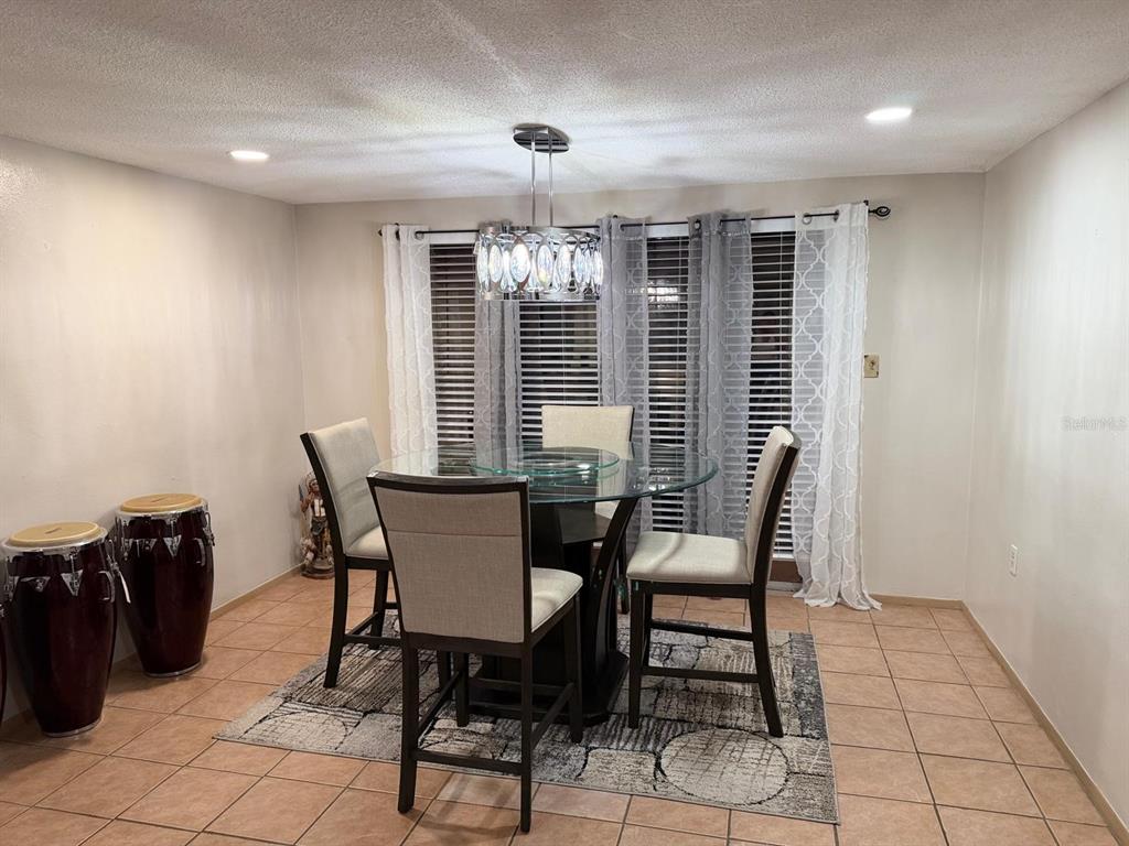 A dining room features a glass-topped table, four upholstered chairs, a crystal chandelier, and conga drums — 9236 GRAY FOX, PORT RICHEY, FL