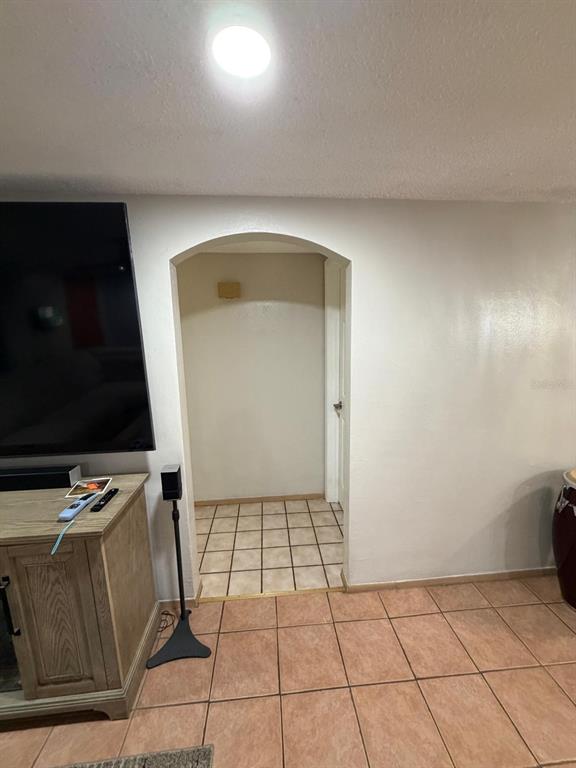 A room with tiled floors features a television console and an arched doorway leading inside — 9236 GRAY FOX, PORT RICHEY, FL