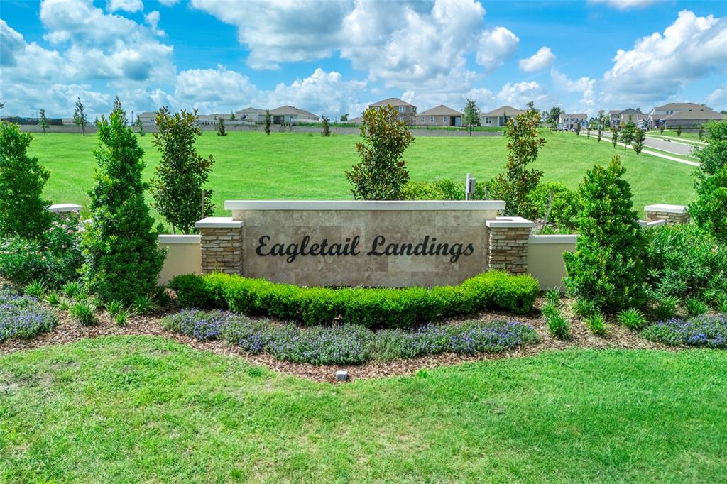 A stone monument sign for Eagletail Landings sits in a grassy field with suburban houses — 6812 BROAD WING LOOP, HOWEY IN THE HILLS, FL