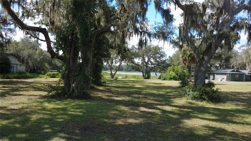 A grassy lot with large oak trees leads to a view of a distant lake — SE HWY 42, WEIRSDALE, FL