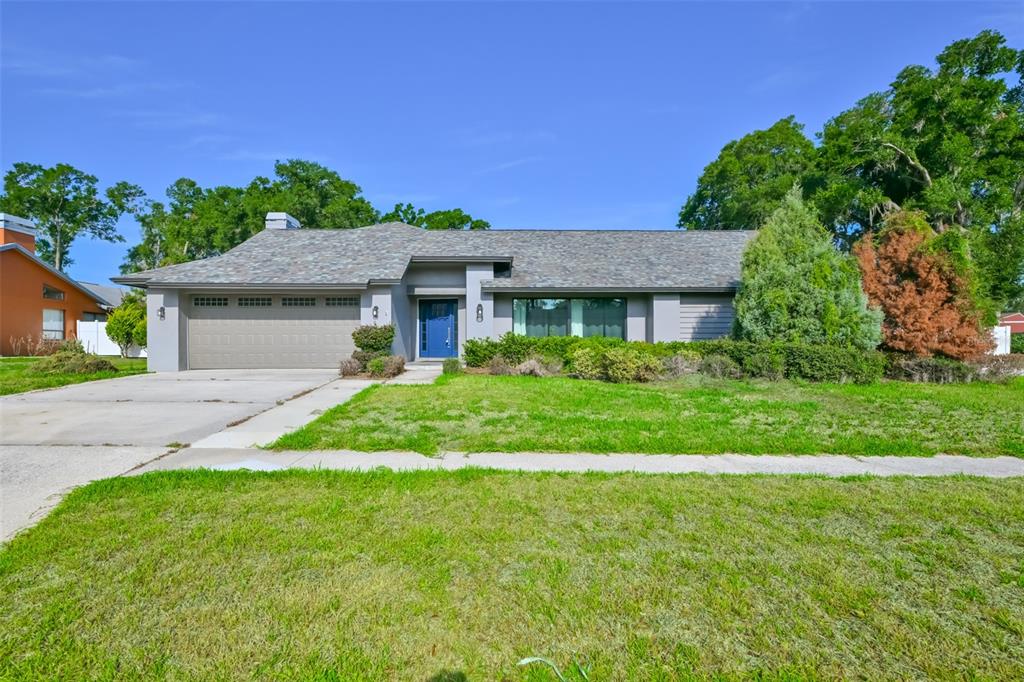 A single-story house with a gray garage, a blue front door, and a landscaped lawn — 2701 HERNDON STREET, VALRICO, FL