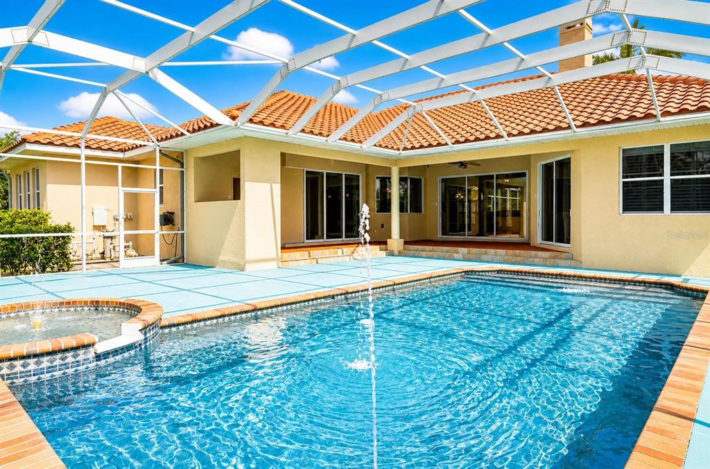 A swimming pool with a fountain sits inside a screened-in lanai behind a house — 6120 9TH AVENUE CIRCLE NE, BRADENTON, FL