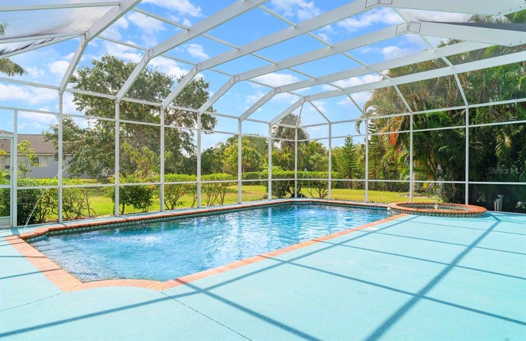 A screened-in swimming pool and spa area with a blue deck and surrounding lush landscaping — 6120 9TH AVENUE CIRCLE NE, BRADENTON, FL