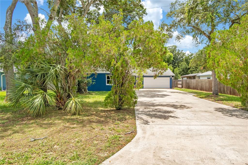 A blue house with a white garage door sits behind trees and a concrete driveway — 236 MCINTOSH ROAD, ORMOND BEACH, FL