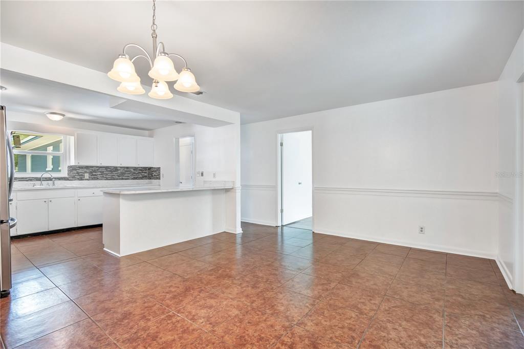 A dining area with brown tile floors and a chandelier opens to a white kitchen — 236 MCINTOSH ROAD, ORMOND BEACH, FL