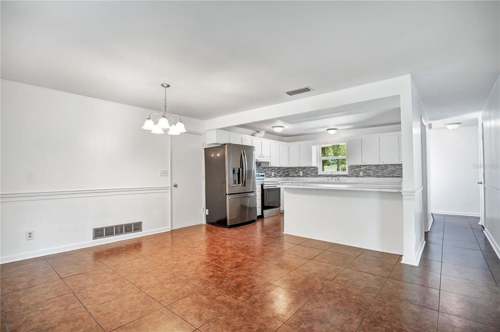 A dining area with tile floors leads into a white kitchen with stainless steel appliances — 236 MCINTOSH ROAD, ORMOND BEACH, FL