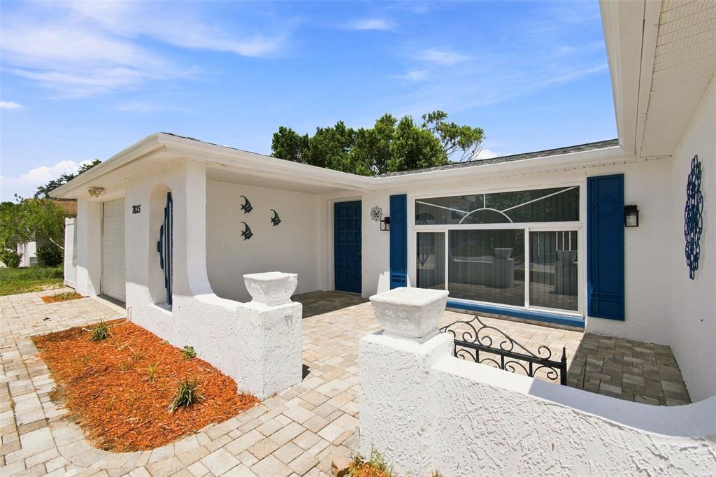 A white house exterior features a paved courtyard, a blue front door, and blue shutters — 7025 WESTCOTT DRIVE, PORT RICHEY, FL