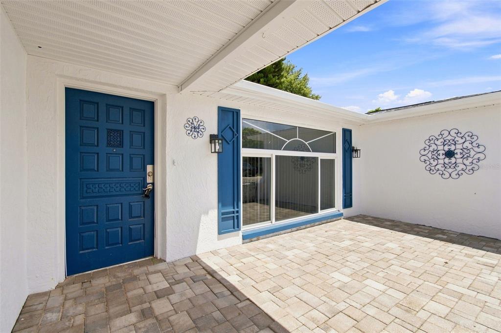 A blue front door and a large window with blue shutters face a paved patio area — 7025 WESTCOTT DRIVE, PORT RICHEY, FL