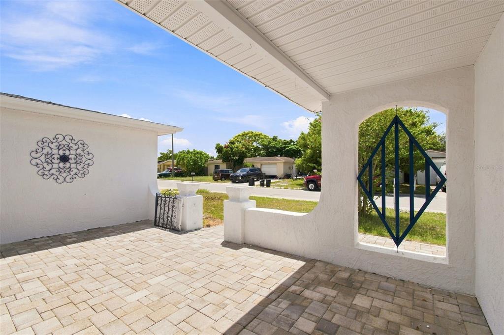 A paved patio area features a white stucco wall, decorative metal accents, and a covered ceiling — 7025 WESTCOTT DRIVE, PORT RICHEY, FL