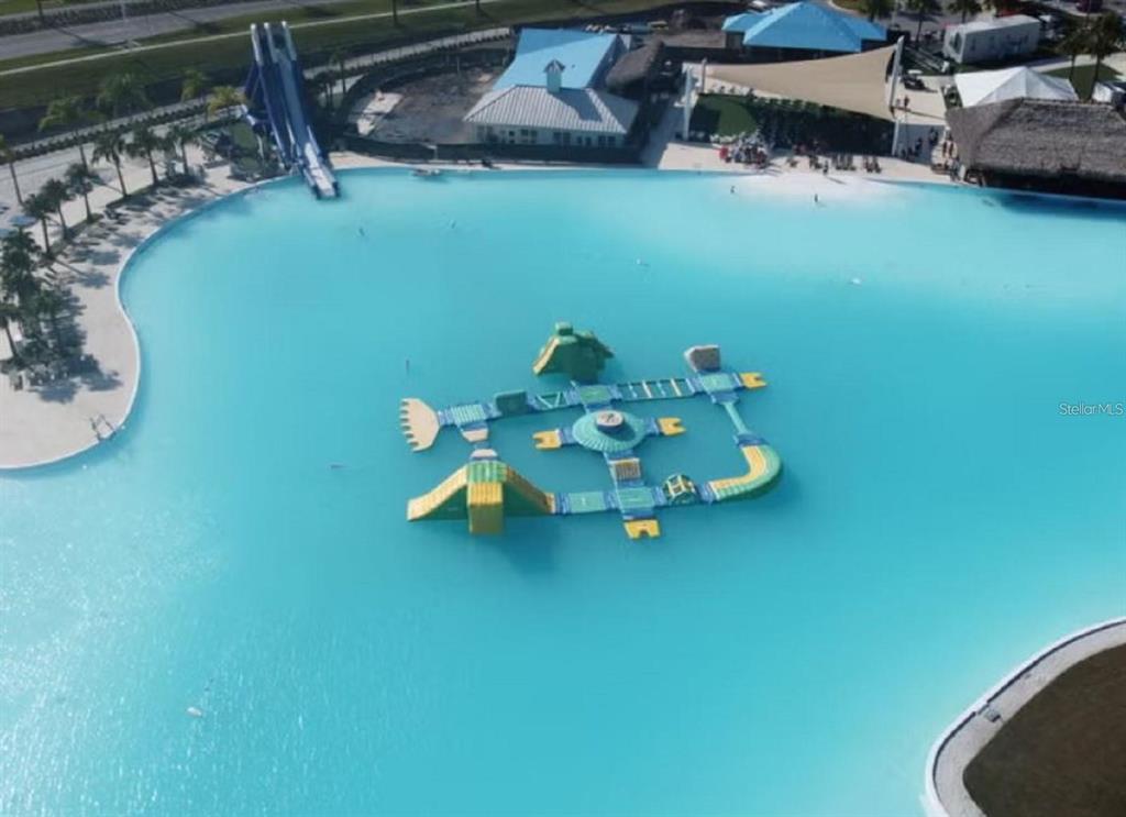 An aerial view shows a large turquoise swimming lagoon with an inflatable obstacle course — 7827 GLEN LILY PLACE, PARRISH, FL