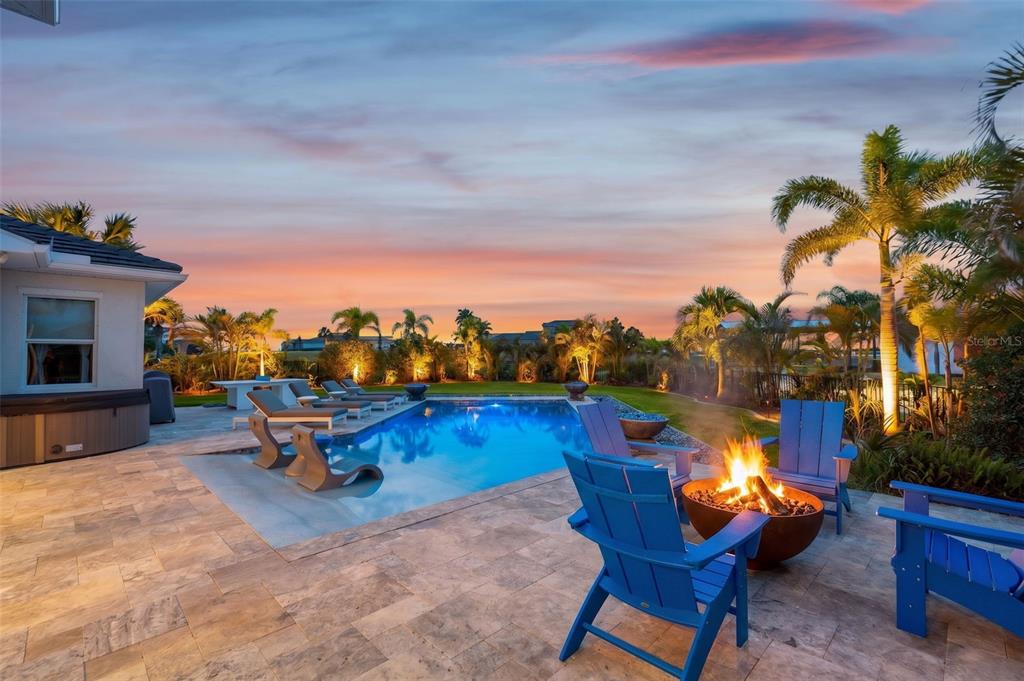 A backyard patio features a swimming pool, fire pit, and blue chairs at sunset — 1256 TYNE LANE, BRADENTON, FL