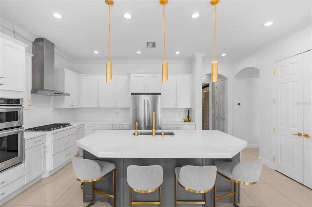 A modern kitchen features white cabinetry, a dark gray island with bar seating, and gold pendants — 1256 TYNE LANE, BRADENTON, FL