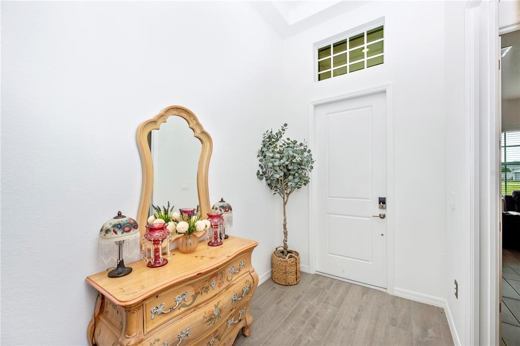 A bright entryway features a wooden dresser with a mirror, a potted plant, and tile flooring — 12845 TULUM LOOP, VENICE, FL