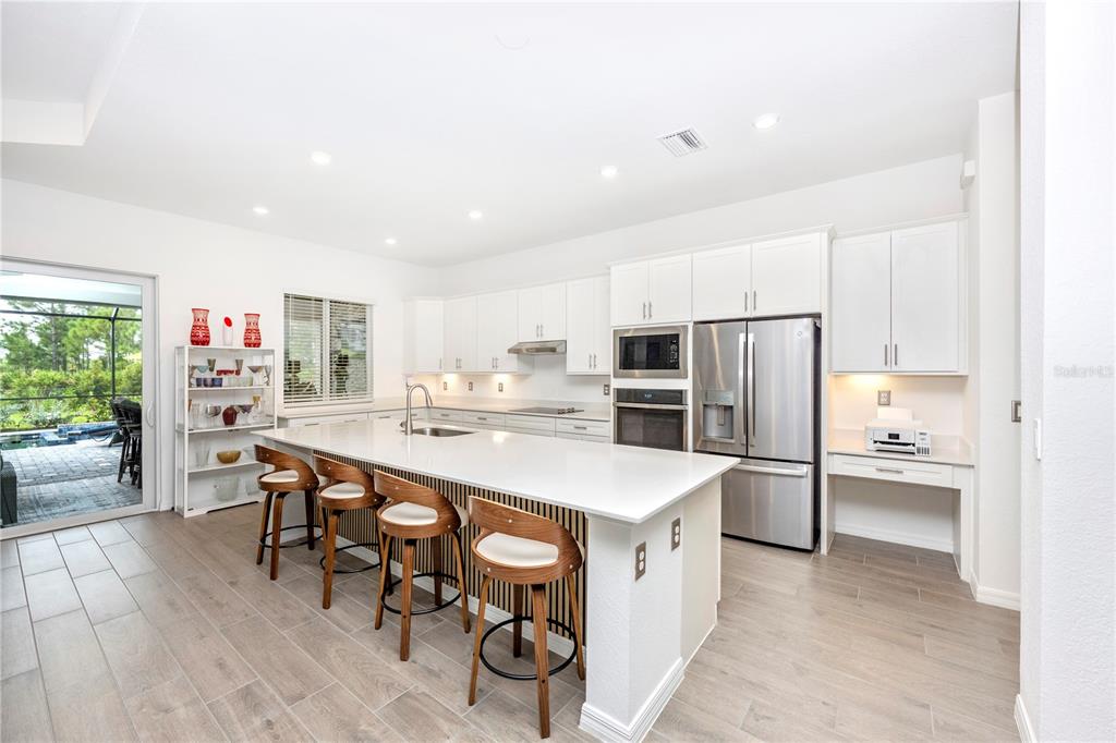 A modern kitchen features a large white island, stainless steel appliances, and light wood-look flooring — 12845 TULUM LOOP, VENICE, FL