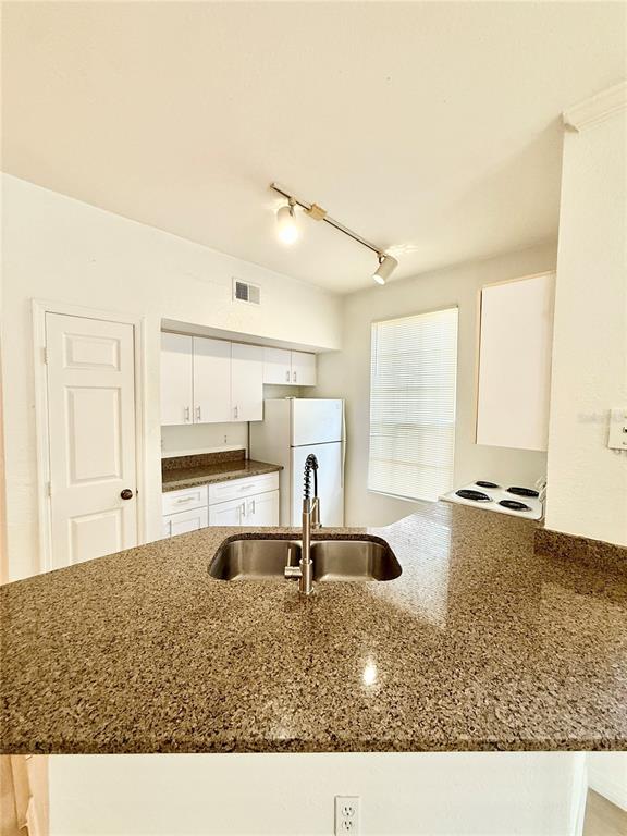 A kitchen features white cabinets, granite countertops, a double sink, and a white refrigerator — 6356 RALEIGH STREET UNIT 1503, ORLANDO, FL