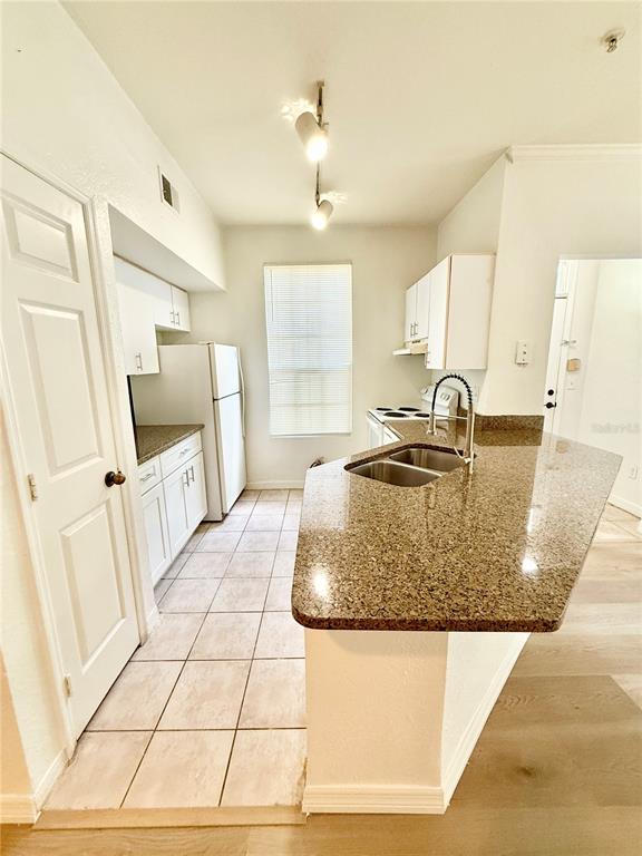 A kitchen features granite countertops, white cabinetry, tile flooring, and a stainless steel sink — 6356 RALEIGH STREET UNIT 1503, ORLANDO, FL