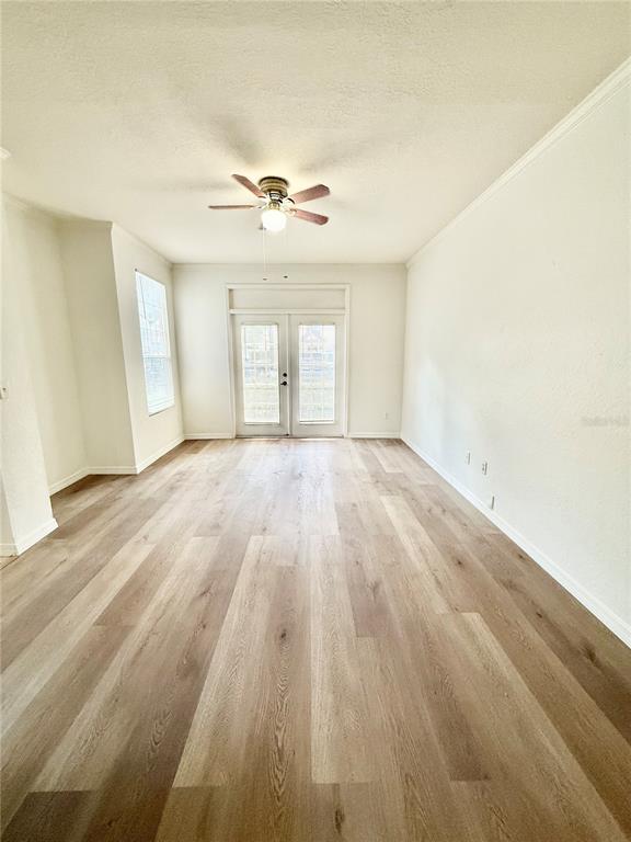 An empty room with light wood-look flooring, a ceiling fan, and glass double doors — 6356 RALEIGH STREET UNIT 1503, ORLANDO, FL