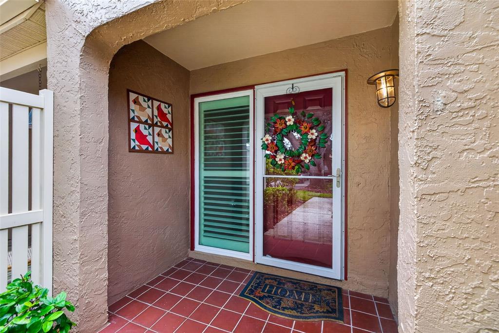 A covered entryway features a tiled floor, a red front door with a wreath, and shutters — 495 ST TROPEZ CIRCLE NE, ST PETERSBURG, FL