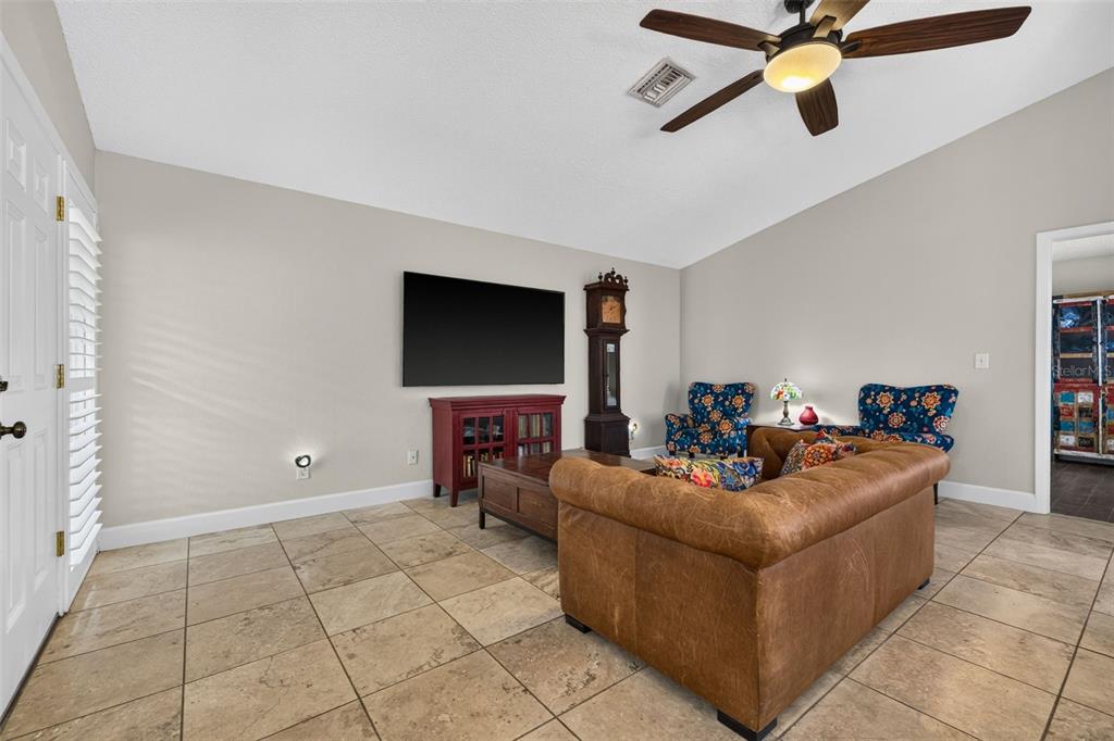 A living room features a brown leather sofa, patterned armchairs, tile flooring, and a ceiling fan — 495 ST TROPEZ CIRCLE NE, ST PETERSBURG, FL