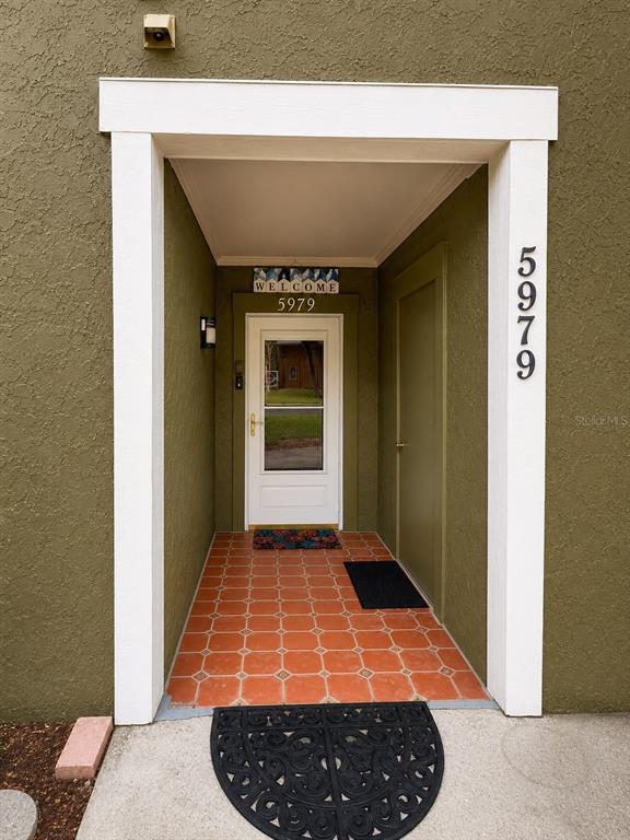 An exterior entryway features a white door, orange tiled floor, and olive green stucco walls — 5979 WINDHOVER DRIVE UNIT 7A, ORLANDO, FL